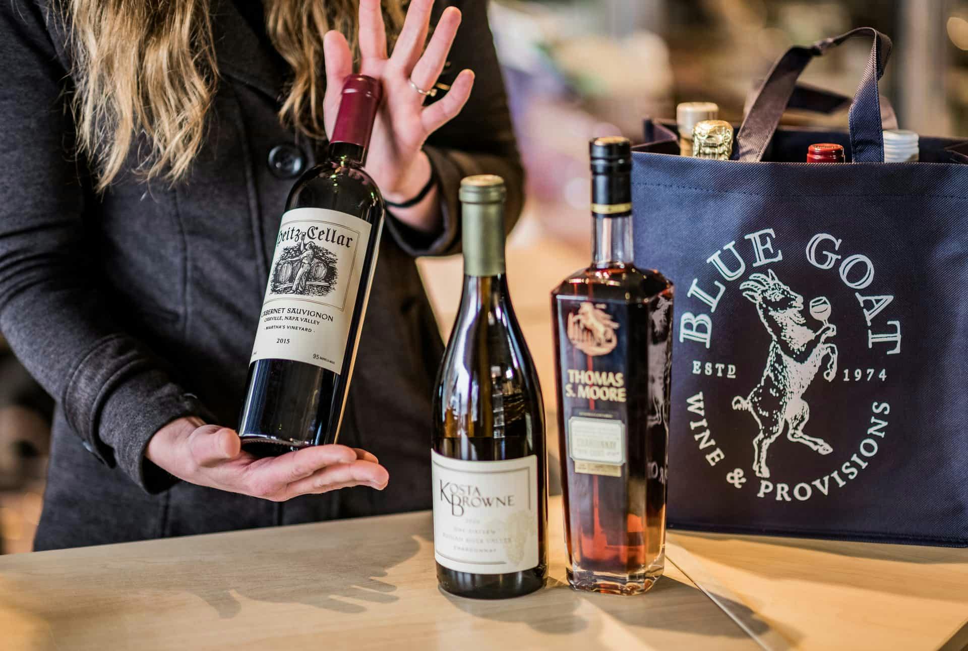 An employee presenting a bottle of wine out of a Blue Goat branded tote bag.