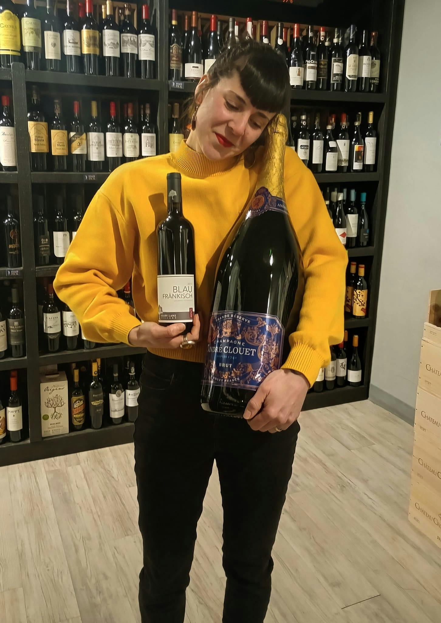 Candace holding a regular sized bottle of wine, as well as a very large bottle of wine.